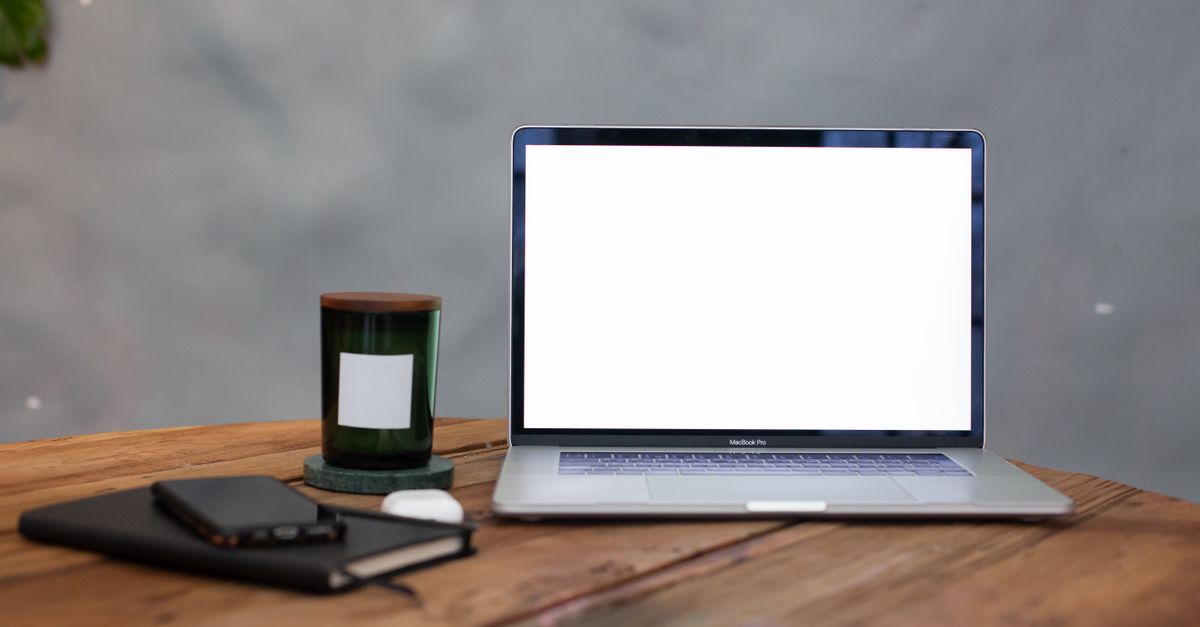 A modern workspace featuring a blank laptop screen, notebook, and candle on a wooden table.