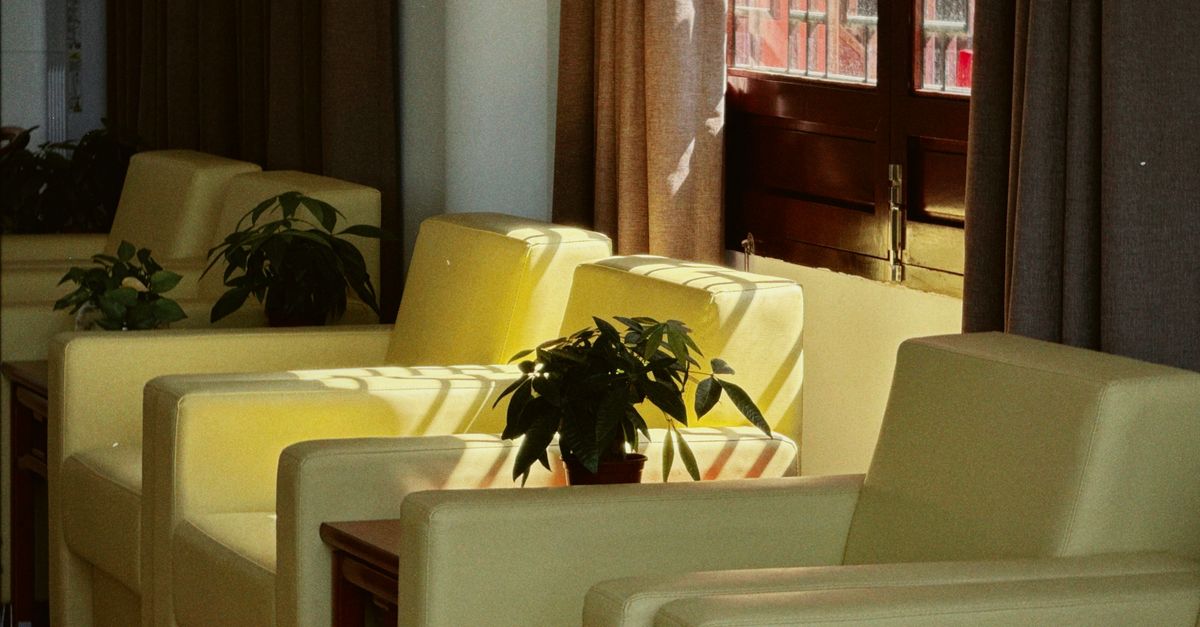 Sunlit corner with a beige armchair and a candle on a wooden table, creating a warm, inviting ambiance.