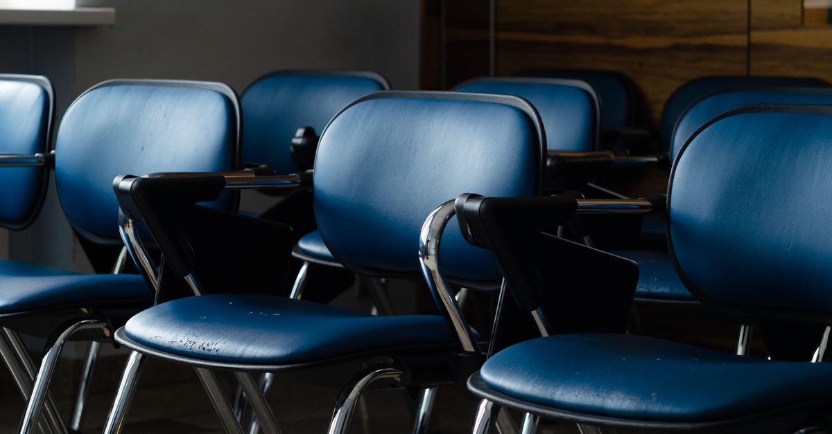 A row of blue desk chairs in a quiet, dimly lit room, ready for use.