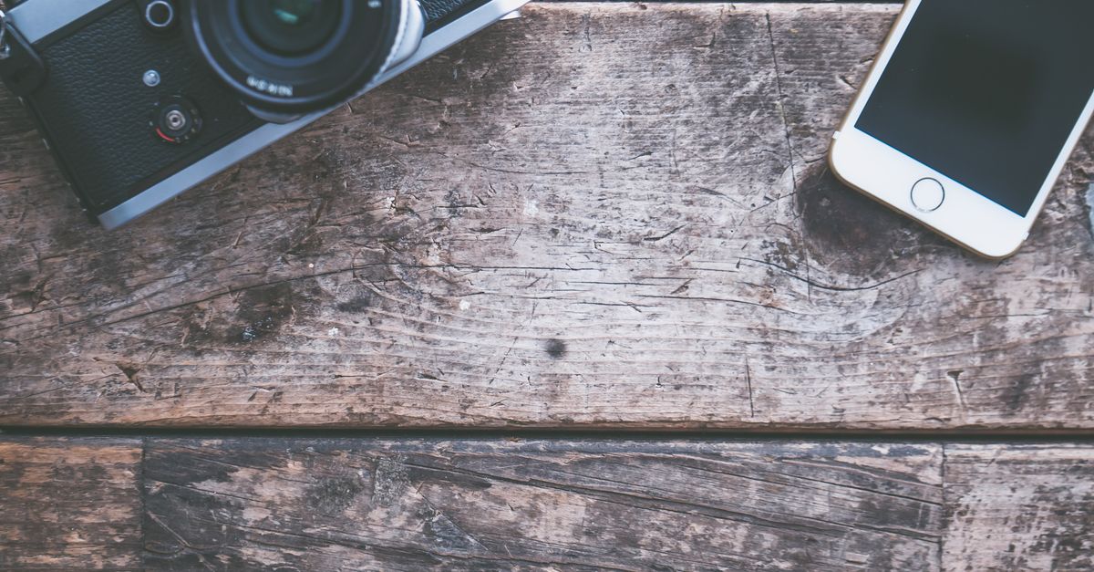 A flat lay of a vintage camera and smartphone on a rustic wooden table, ideal for tech and photography themes.