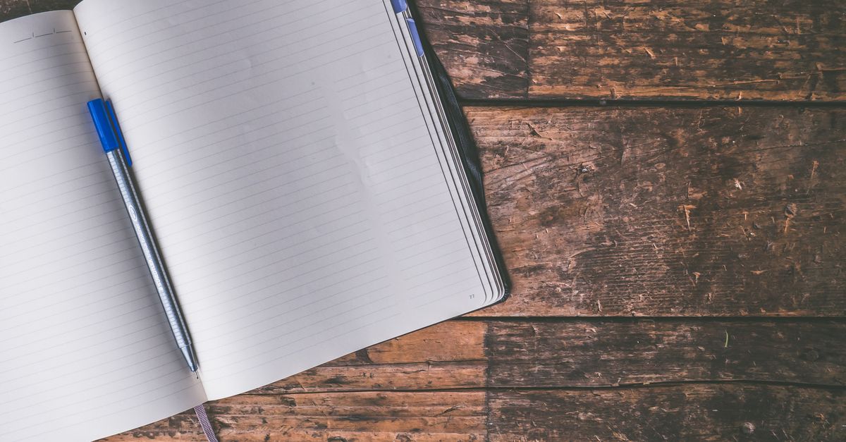 An open notebook with a blue pen lies on a rustic wooden table, inviting creativity and writing.