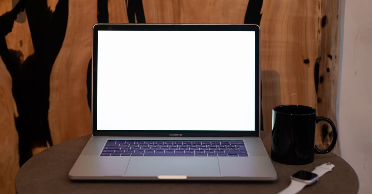 A contemporary workspace featuring a laptop with blank screen, coffee mug, and smartwatch on a table.