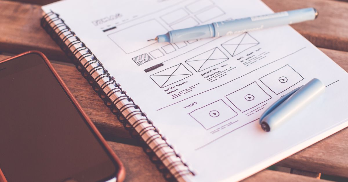 Close-up of a notebook with wireframe sketches and a smartphone on a wooden desk.